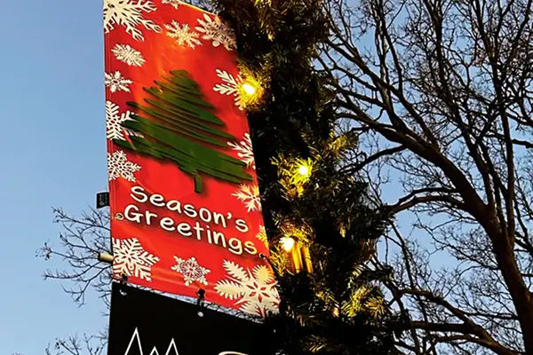 “Season's Greetings” street pole banner with lit garland for retail district decoration